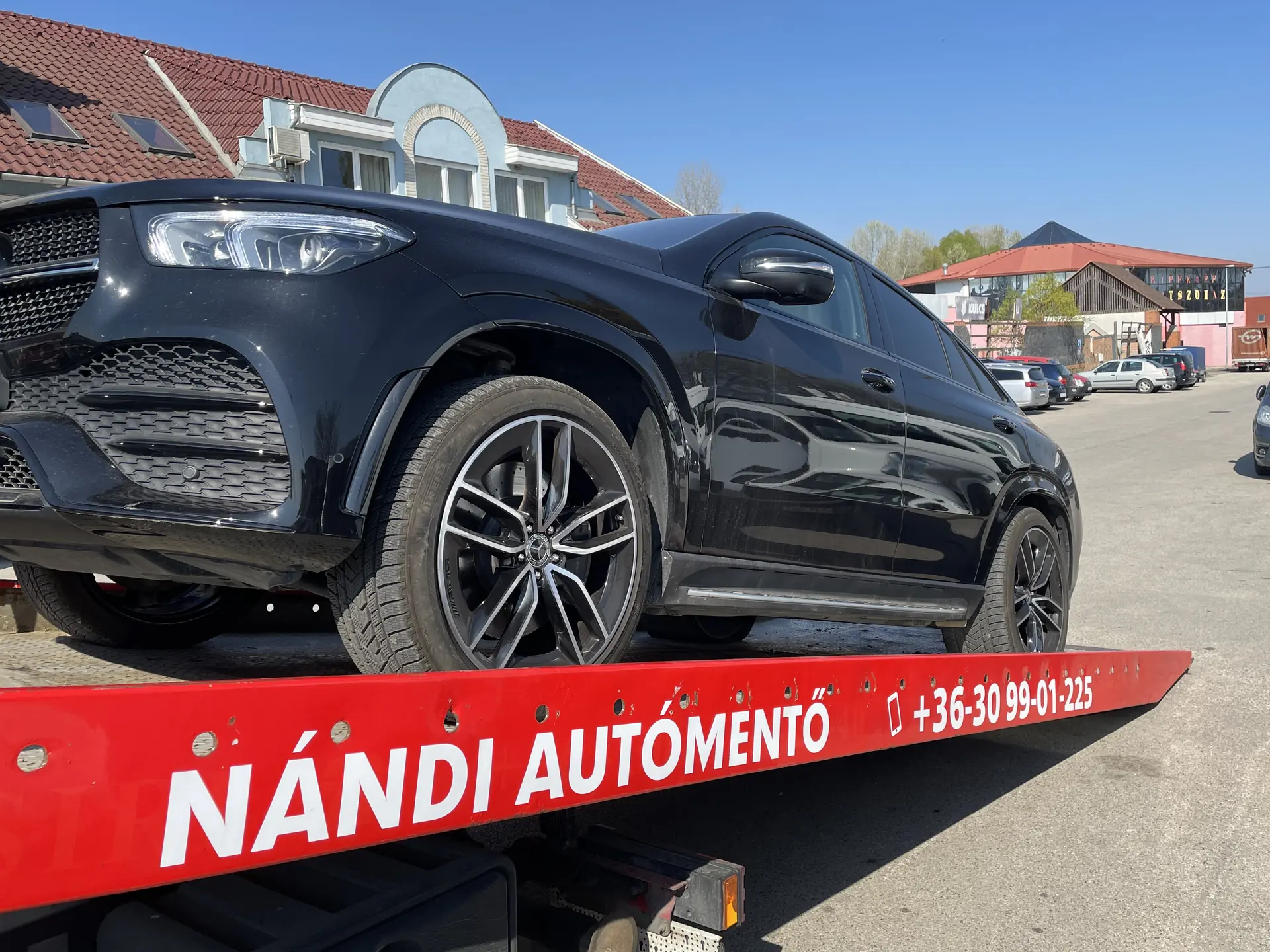 Fekete Mercedes GLE Coupé Nándi trélerén, a platón a Nándi autómentő felirat és a telefonszám Fekete Mercedes GLE Coupé Nándi trélerén, a platón a Nándi autómentő felirat és a telefonszám