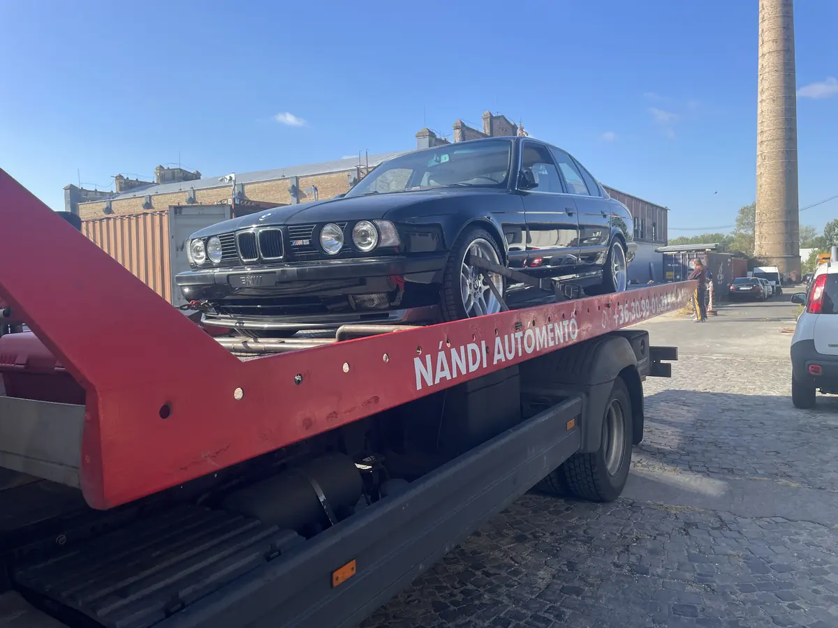 Sötétkék BMW M5 (E34) Nándi trélerén, a platón a Nándi autómentő felirat